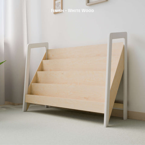 The image shows a large Montessori-style bookshelf made of natural wood with a white wood finish on the frame. The bookshelf has multiple tiers designed for front-facing book display, fitting well in a light-colored, softly lit room. The minimalist design promotes a clean and organized space ideal for a child's play area or bedroom. The combination of natural wood and white finish enhances the serene and inviting atmosphere, adding a modern touch to the room.