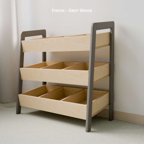 The image displays an empty Montessori-style toy organizer with a grey and natural wood finish. The organizer features three tiers of open bins made of natural wood, framed by grey-painted sides. This practical and minimalist design is perfect for organizing children's toys and books, encouraging easy access and tidy habits. Positioned against a light-colored wall in a softly lit room, the organizer adds a modern and clean touch to the space.