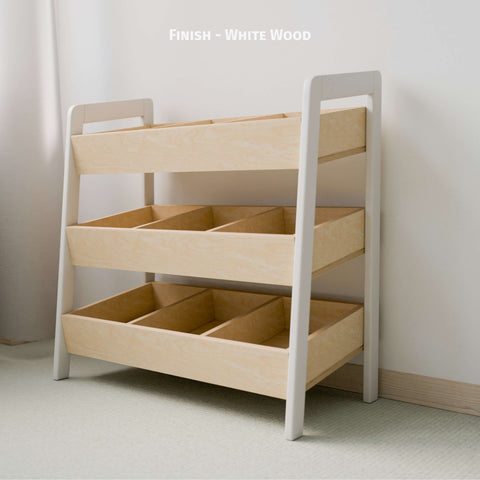  The image features an empty Montessori-style toy organizer with a white and natural wood finish. The organizer consists of three tiers of open bins made of natural wood, framed by white-painted sides. This minimalist design is ideal for organizing children's toys and books, promoting easy access and tidy habits. The piece is placed against a light-colored wall in a softly lit room, enhancing its clean and modern aesthetic.