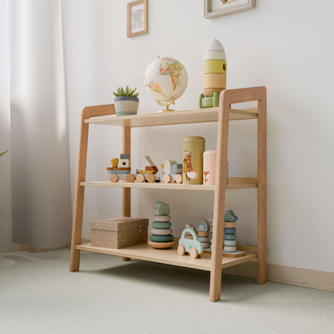 A neat and well-organized children's play area with a wooden toy storage rack. The rack holds various Montessori-style toys including wooden blocks, a stacking tower, cars, and a decorative globe. The space is bright with natural light, enhancing the calm and inviting atmosphere.