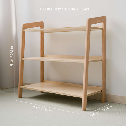 The image features a wooden three-level toy storage shelf displayed against a clean, light-colored wall, with dimensions labeled on the image. The top height of the shelf is noted as 75 cm (29.5 in), the width is 74 cm (29.1 in), and the depth is 35 cm (13.94 in). The design is minimalistic with a focus on the natural wood finish, suitable for a Montessori-style room setup. The environment is softly lit, contributing to a warm and inviting atmosphere.