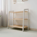 The image shows a three-tiered toy storage shelf featuring a white and natural wood finish. The legs of the shelf are painted white, contrasting with the natural wooden shelves. The background is a clean, light-colored wall in a room that appears to be softly lit by natural light, providing a serene and organized space ideal for a children's play area or a minimalist home decor. Text on the image indicates the finish as "White Wood."