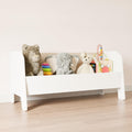 Modern montessori toy chest with white sides and wooden interior, filled with toys.