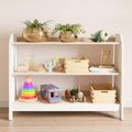 Wide montessori toy storage with three shelves, it has white sides and wooden shelves on which children's toys are arranged.