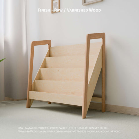 The image shows  Montessori-style bookshelf made of raw or varnished natural wood. The bookshelf has multiple tiers designed for easy display and access to children's books or toys. The minimalist design fits well in a light-colored, softly lit room, promoting a clean and organized space ideal for a child's play area or bedroom.