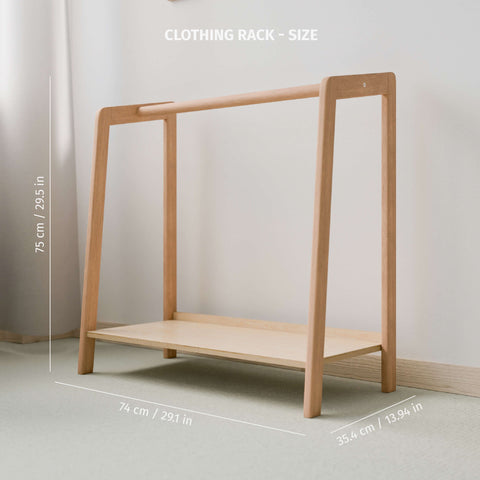 The image features an empty Montessori-style clothing rack made of natural wood, highlighting its dimensions. It stands 75 cm (29.5 inches) tall, 74 cm (29.1 inches) wide, and 35.4 cm (13.94 inches) deep. The design is minimalistic and functional, with a flat shelf at the bottom for additional storage, such as shoes or baskets. The light wood tone of the rack contrasts softly against a neutral wall, creating a calm and orderly environment, perfect for a child's room or play area.