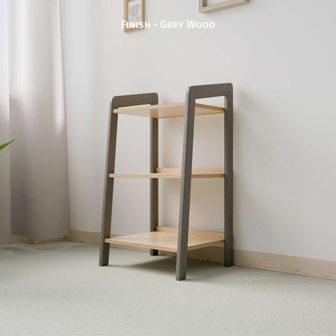 The image features an empty small Montessori-style toy storage shelf with a grey and natural wood finish. The shelf has three tiers, providing ample space for organizing children's toys and items. The frame is painted grey, while the shelves maintain their natural wood look, creating a sleek and modern aesthetic. Positioned against a light-colored wall in a softly lit room, the minimalist design enhances the clean and organized atmosphere, making it an ideal addition to a child's play area or bedroom.