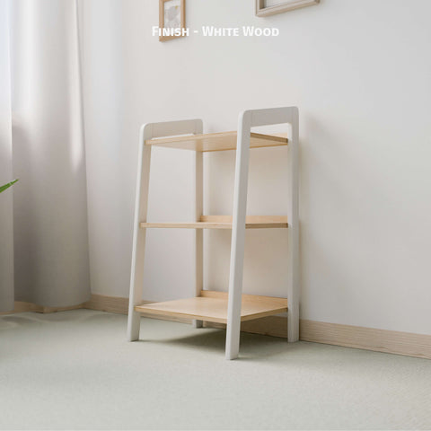 The image showcases an empty small Montessori-style toy storage shelf with a white and natural wood finish. The shelf features three tiers, offering ample space for organizing children's toys and items. The frame is painted white, while the shelves retain their natural wood look, creating a clean and modern aesthetic. Positioned against a light-colored wall in a softly lit room, the minimalist design enhances the bright and organized atmosphere, making it an ideal addition to a child's play area or bedroom.