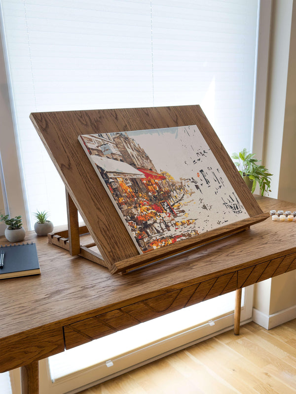 Adjustable wooden desk easel displaying a painting canvas on a desk in a sunny workspace