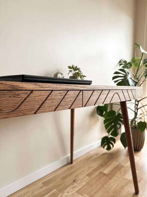Close-up of a solid wood desk with geometric carved details and a closed laptop in a home office setting.