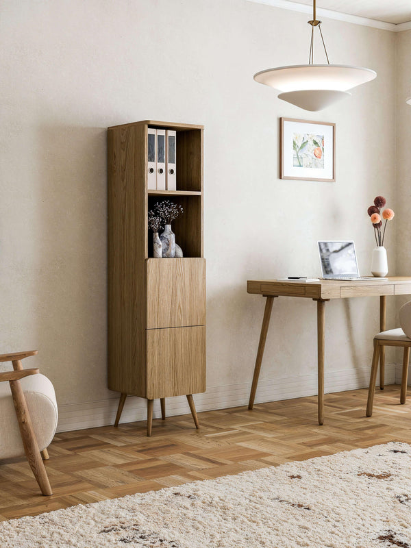 Tall oak veneer storage cabinet with two drawers and open shelves, styled in a mid-century home office with matching desk and natural lighting.