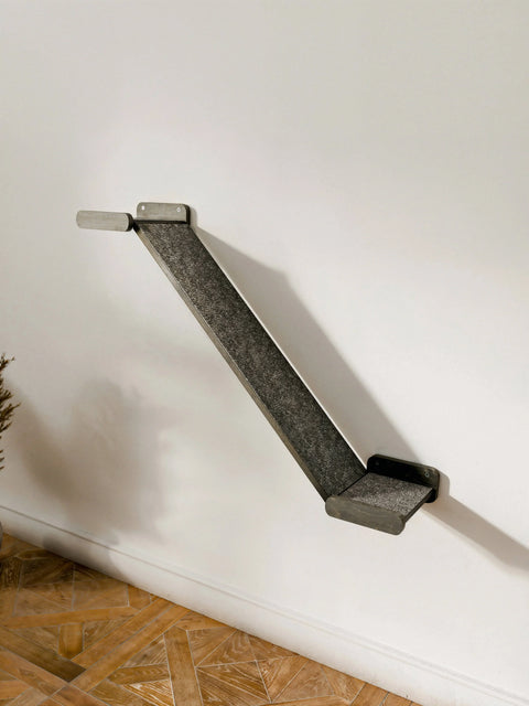 Side view of a single Minimalist Cat Bridge installed on a white wall, featuring dark wood finish brackets and a grey felt ramp surface. A functional Wall-Mounted Cat Climber setup in a dark color option.