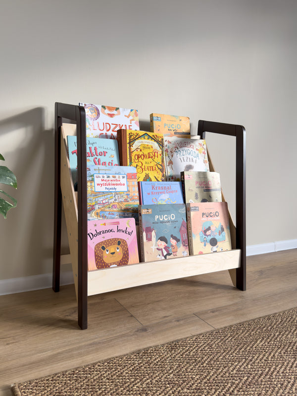 Montessori-style floor bookshelf featuring a dark wood frame and natural shelving, filled with colorful children's books and placed on a wooden floor with a woven rug.