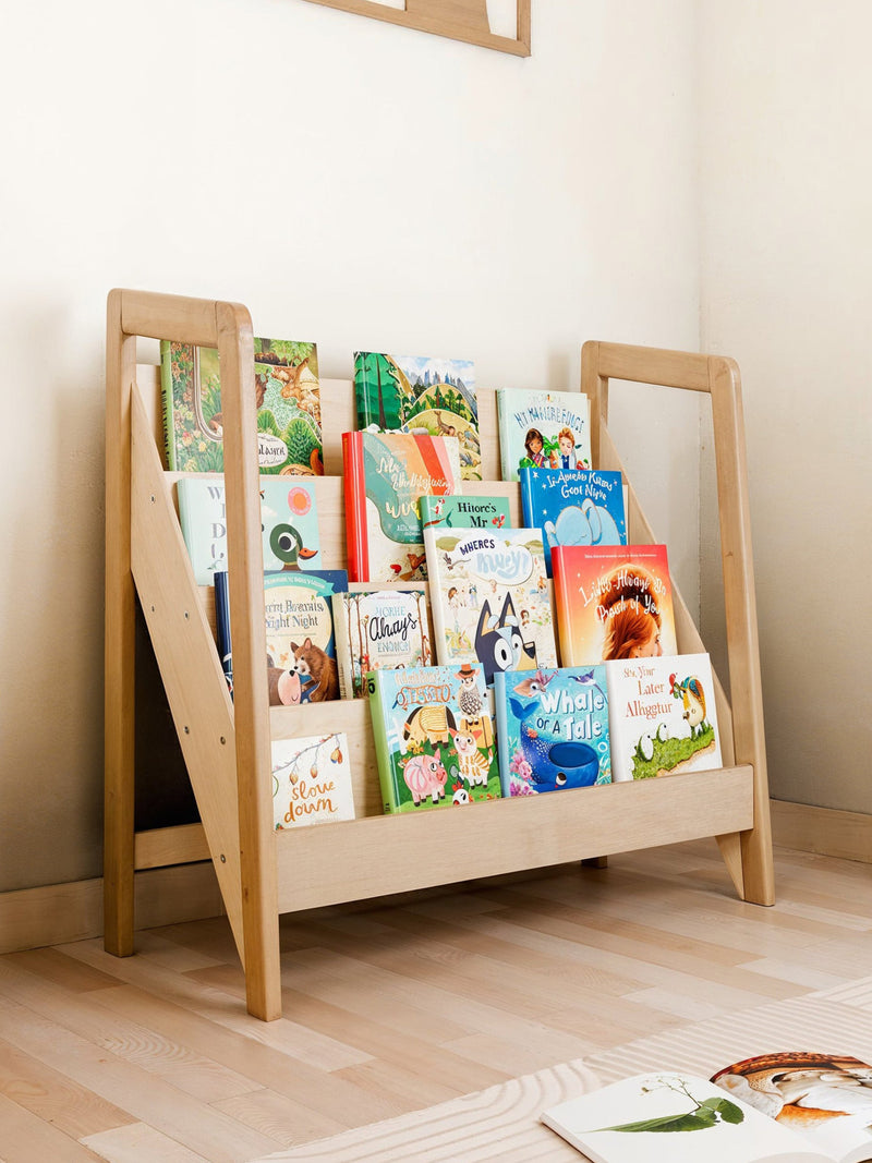 Wooden Montessori bookshelf with forward-facing book display filled with colorful children's books in a nursery