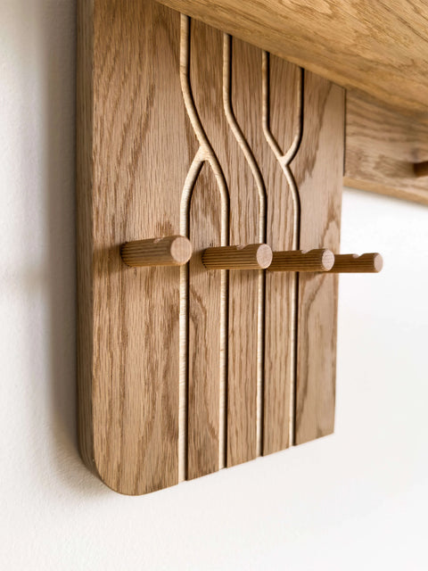 Macro detail of the oak entryway organizer showing the natural wood grain and carved grooves. Focus on the smooth finish of the small wooden hooks designed for keys.
