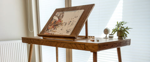 Solid wood desk featuring an adjustable tabletop drawing board with a canvas. An inspiring workspace setup for painting and creative hobbies featuring natural wood furniture.