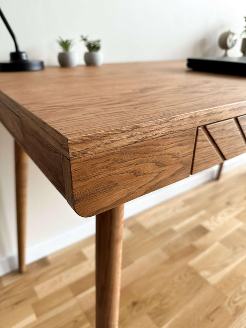 Close-up view of a solid wood desk corner, highlighting the natural grain texture, smooth rounded edges, and handcrafted geometric drawer detail.