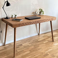 Solid wood desk with geometric carved front details and tapered legs, styled with a laptop and lamp in a modern home office.