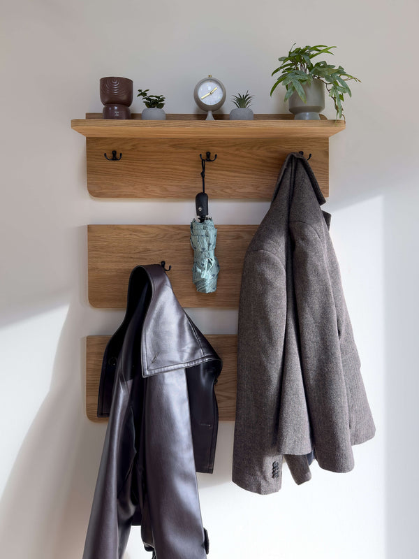 Solid wood wall coat rack with shelf in natural oak finish featuring three panels and eight hooks holding coats and umbrella in an entryway setting