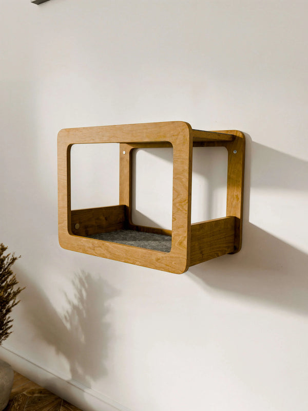 rown wood Wall-Mounted Cat House with a grey felt cushion installed on a white wall. A minimalist Floating Bed for Cats featuring a wide open front design for easy access.