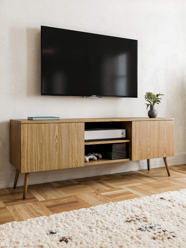 Wooden TV console cabinet with two doors and open shelves, styled in a minimalist living room with mounted screen and oak flooring.